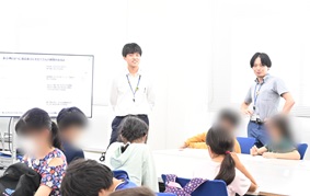 写真:子どもたちが、職員の説明を聞きながらクイズに書き込んでいる様子